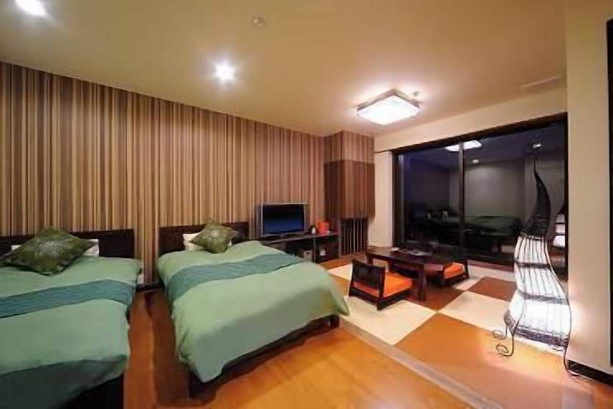 Habitación de hotel con dos camas, televisión, escritorio y ventana grande.