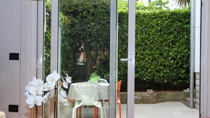Puerta de vidrio que da a un patio exterior con una mesa y sillas, rodeado de un seto.