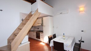 Una cocina con una escalera de madera, una mesa de comedor con sillas y una lámpara de pared.