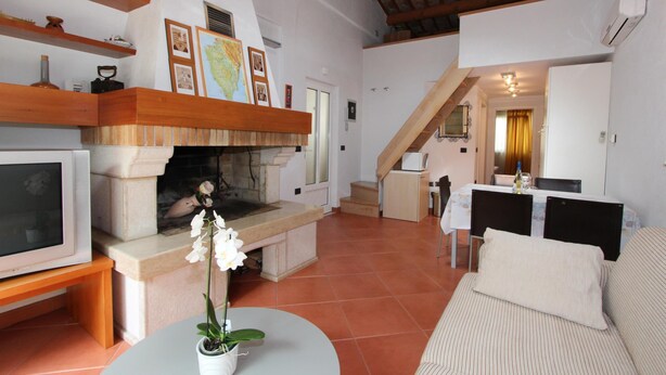 Un salón acogedor con chimenea, televisor y sofá. Una escalera conduce a otra habitación.