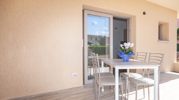 A patio with a table and chairs, a sliding glass door, and a potted plant. - Aria di Vacanza - S'Abba Lughente Trilo (Olbia)