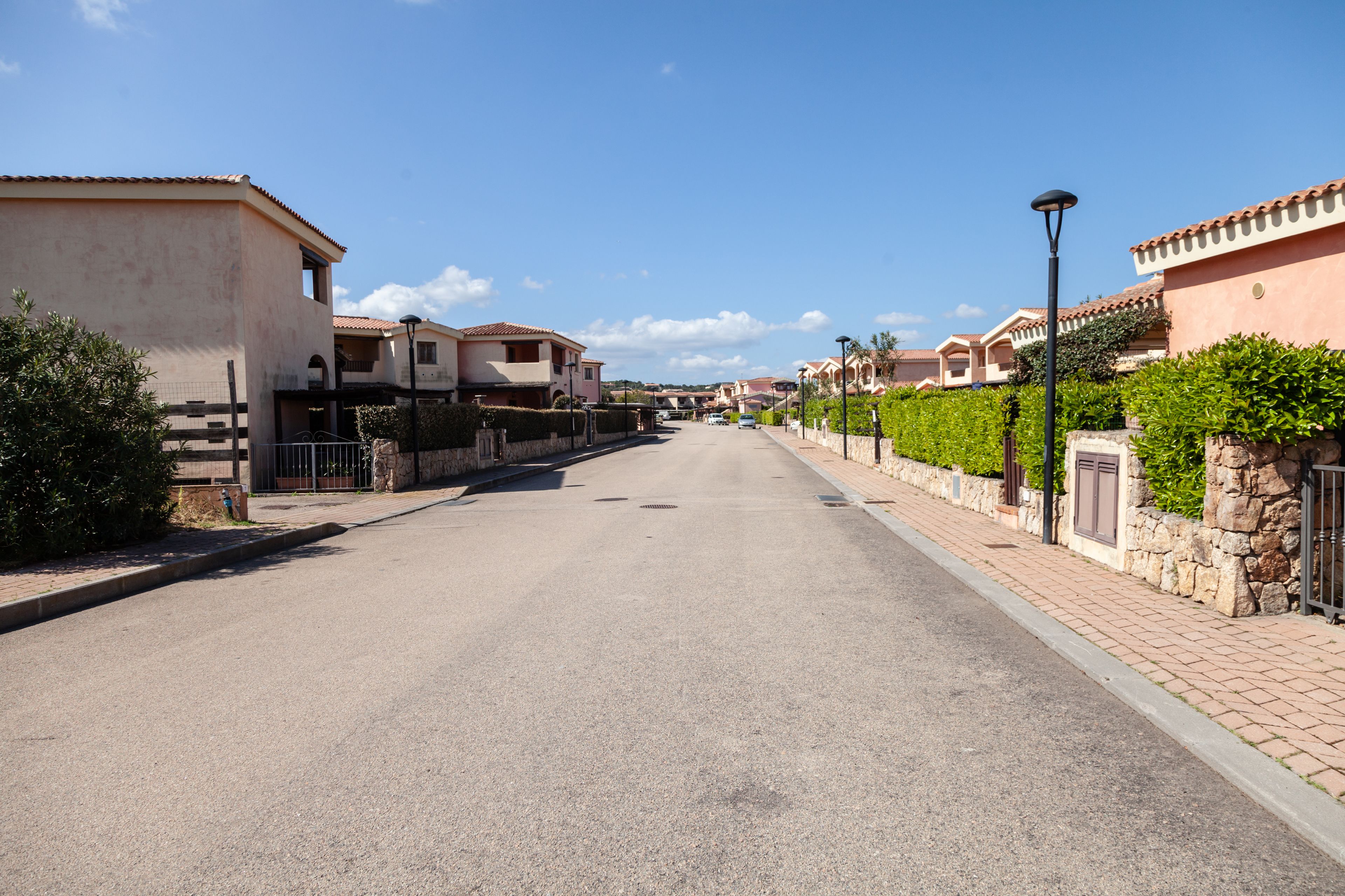 A quiet residential street with houses featuring red-tiled roofs and stucco walls.