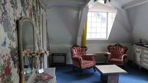 Een kamer met een grote spiegel, twee roze fauteuils, een tafeltje en een raam met een geel gordijn.