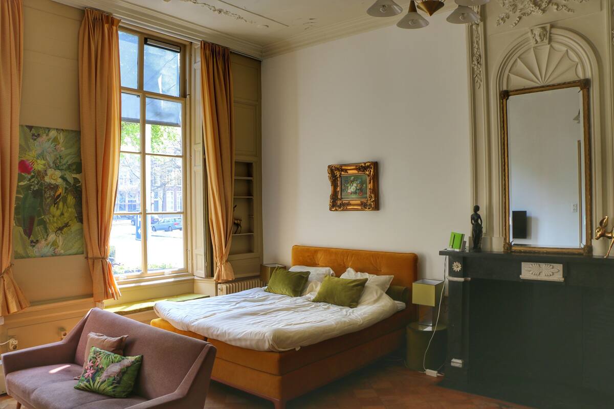 Un dormitorio con cama, una silla, cómoda y ventana con cortinas.