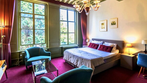 Een hotelkamer met een groot bed, twee fauteuils, een kleine tafel en een kroonluchter.