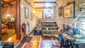 Un couloir étroit avec un mur en pierre, des poutres en bois, un escalier et un lit dans la pièce adjacente.