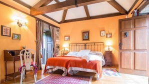 Une chambre avec un plafond en bois, un lit recouvert d’une couverture orange, un bureau avec une chaise et une porte dotée d’une poignée décorative.