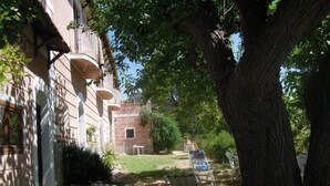 Ein Innenhof mit zwei Liegestühlen, einem großen Baum und einem Gebäude mit Strohdach und Steinmauern.