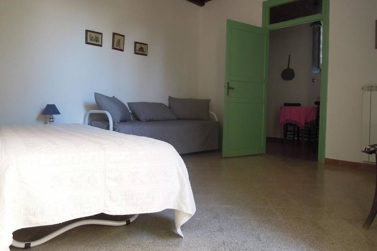 A bedroom with a bed, a green door, and a small table with a lamp.