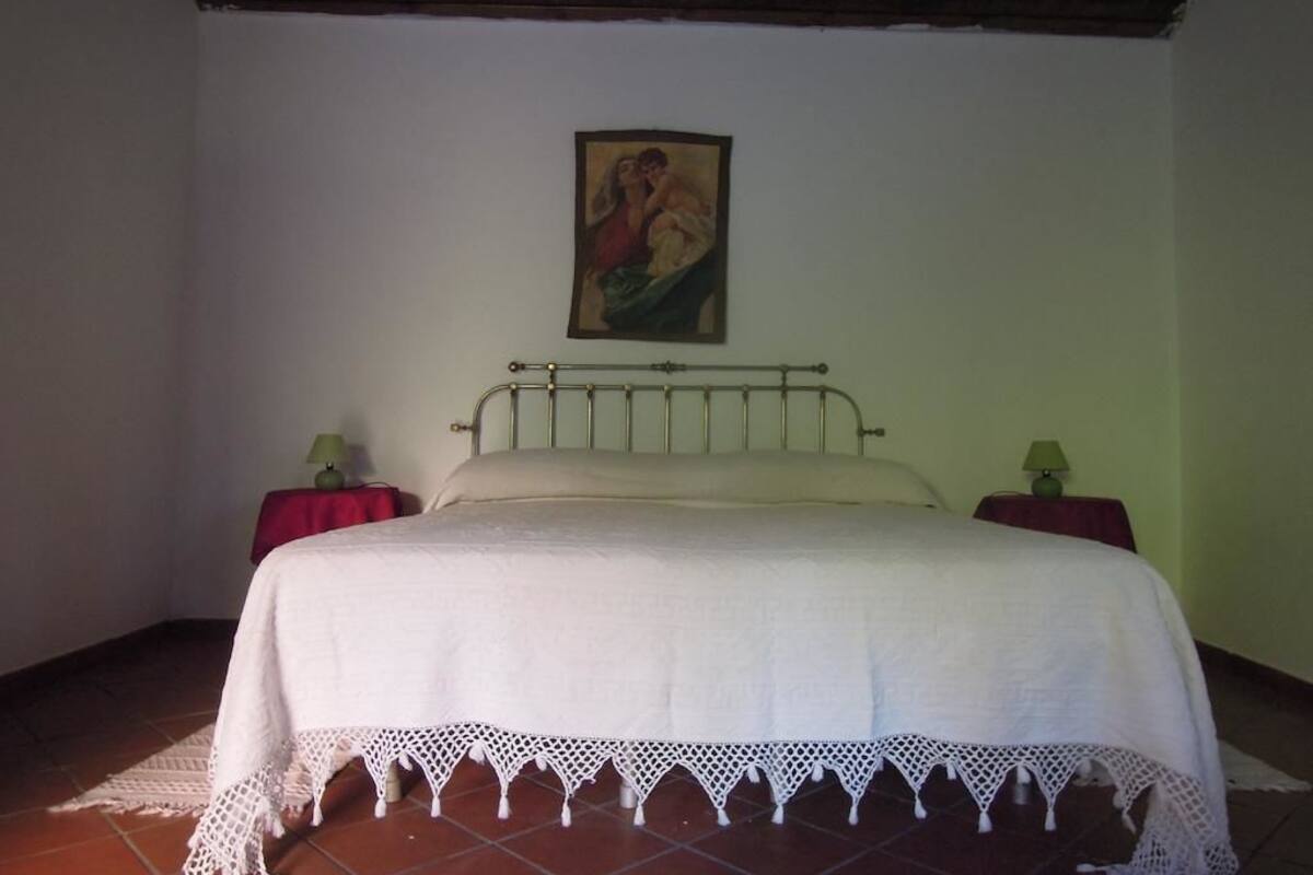 A bedroom with a bed, two bedside tables, a wall-mounted painting, and a red curtain.