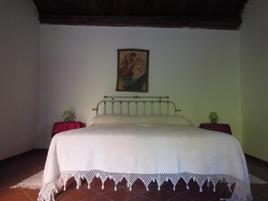 A bedroom with a bed, two bedside tables, a wall-mounted painting, and a red curtain.