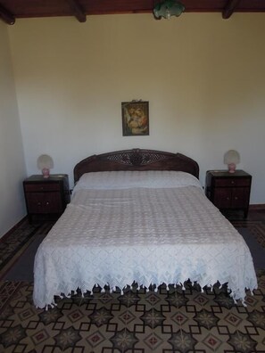 A bedroom with a large bed, two nightstands, a wall hanging, and patterned flooring.