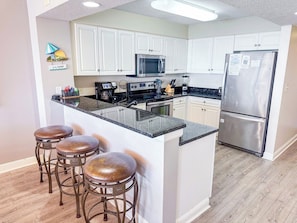 A kitchen with white cabinets, a stainless steel refrigerator, a microwave, and a coffee maker. There are three stools at the island.