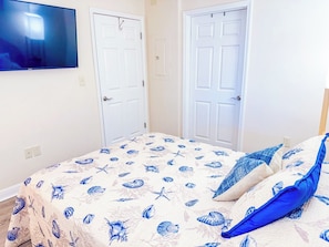 A bedroom with a bed, two white doors, and a wall-mounted television.