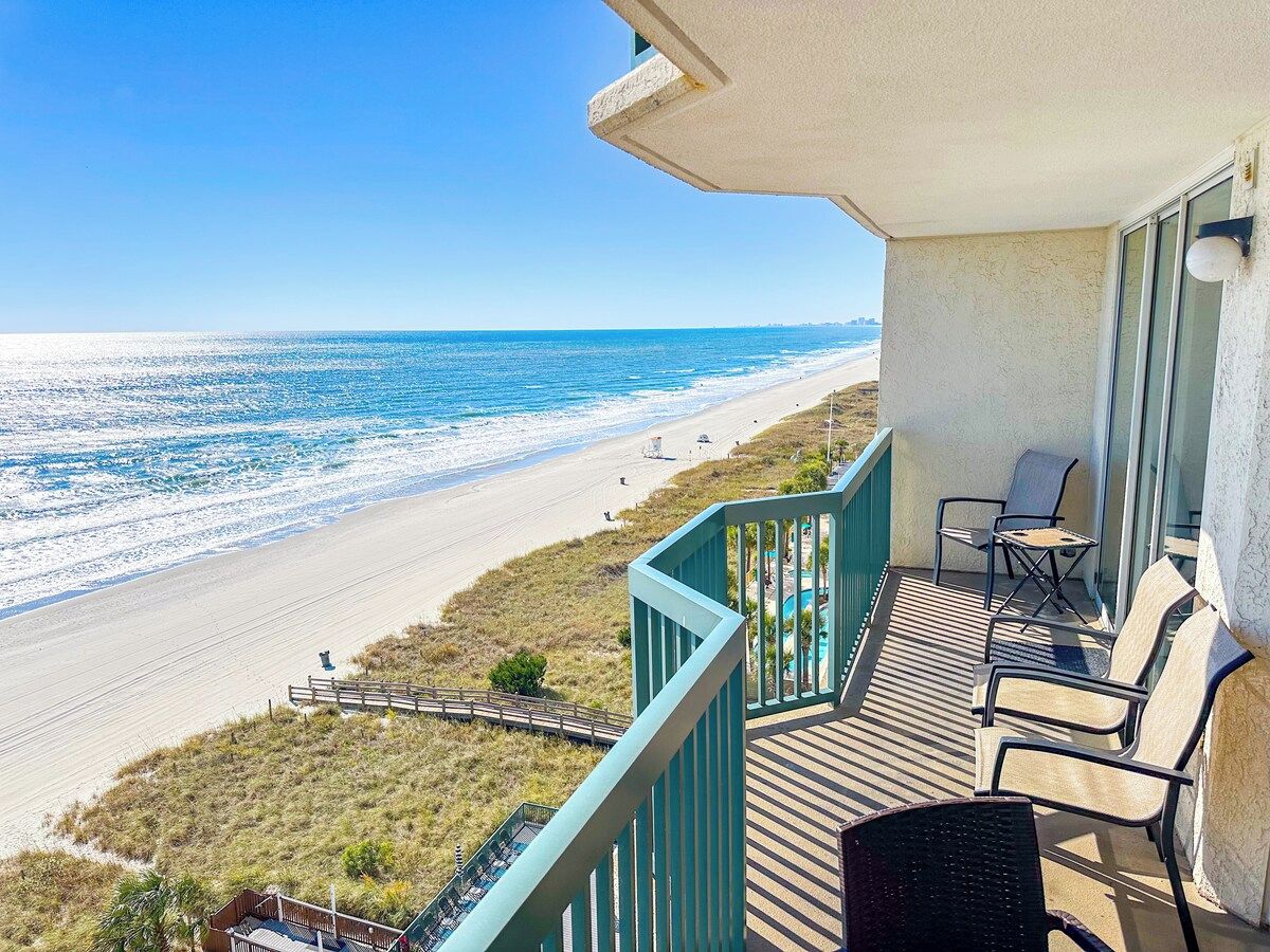 Un balcon avec vue sur la plage, des meubles d’extérieur et une rambarde.