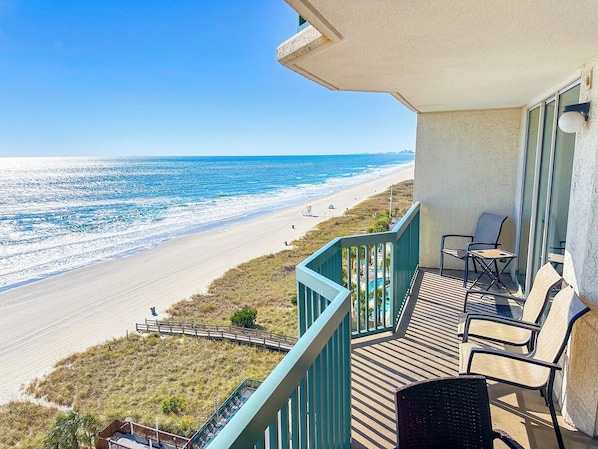 A balcony with a view of the beach, outdoor furniture, and a railing.