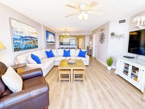 A living room with a sofa, a coffee table, a television, and a ceiling fan.