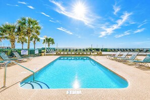 A swimming pool with lounge chairs and palm trees, surrounded by a fence.