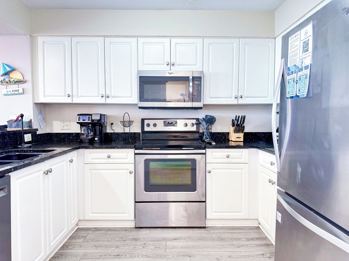 Una cocina moderna con armarios blancos, horno de acero inoxidable, microondas y refrigerador.