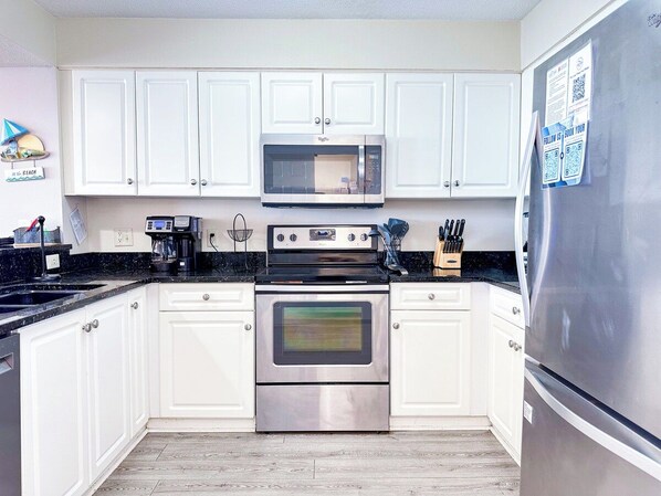 Una cocina moderna con armarios blancos, horno de acero inoxidable, microondas y refrigerador.
