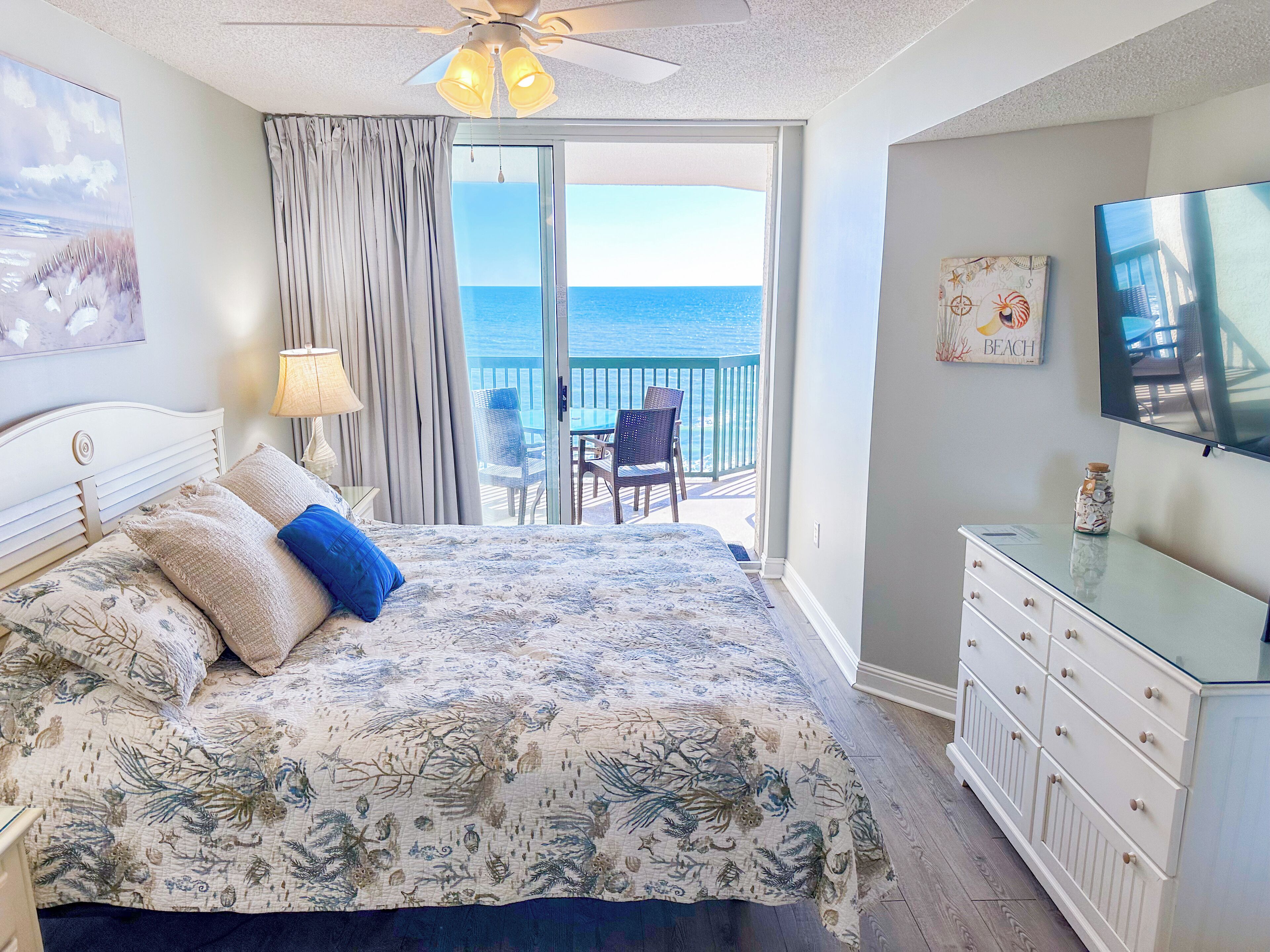 Quarto com cama, televisão, cômoda e varanda com vista para o oceano.