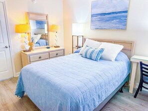 Un dormitorio con cama, mesita de noche, lámpara, cómoda y un cuadro en la pared.