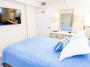 A bedroom with a bed, a dresser, a mirror, and a television.