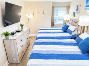 Un dormitorio con dos camas, un televisor, un aparador y una ventana con cortinas.