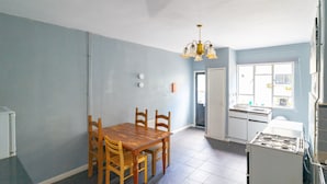 A dining area with a wooden table and chairs, a chandelier, and a kitchen with a stove. - Stag and Hen Friendly House (Bath)