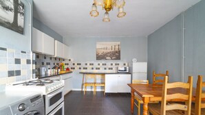 A compact kitchen with a stove, oven, and washing machine, wooden dining table and chairs, a microwave, and a tiled backsplash. - Stag and Hen Friendly House (Bath)