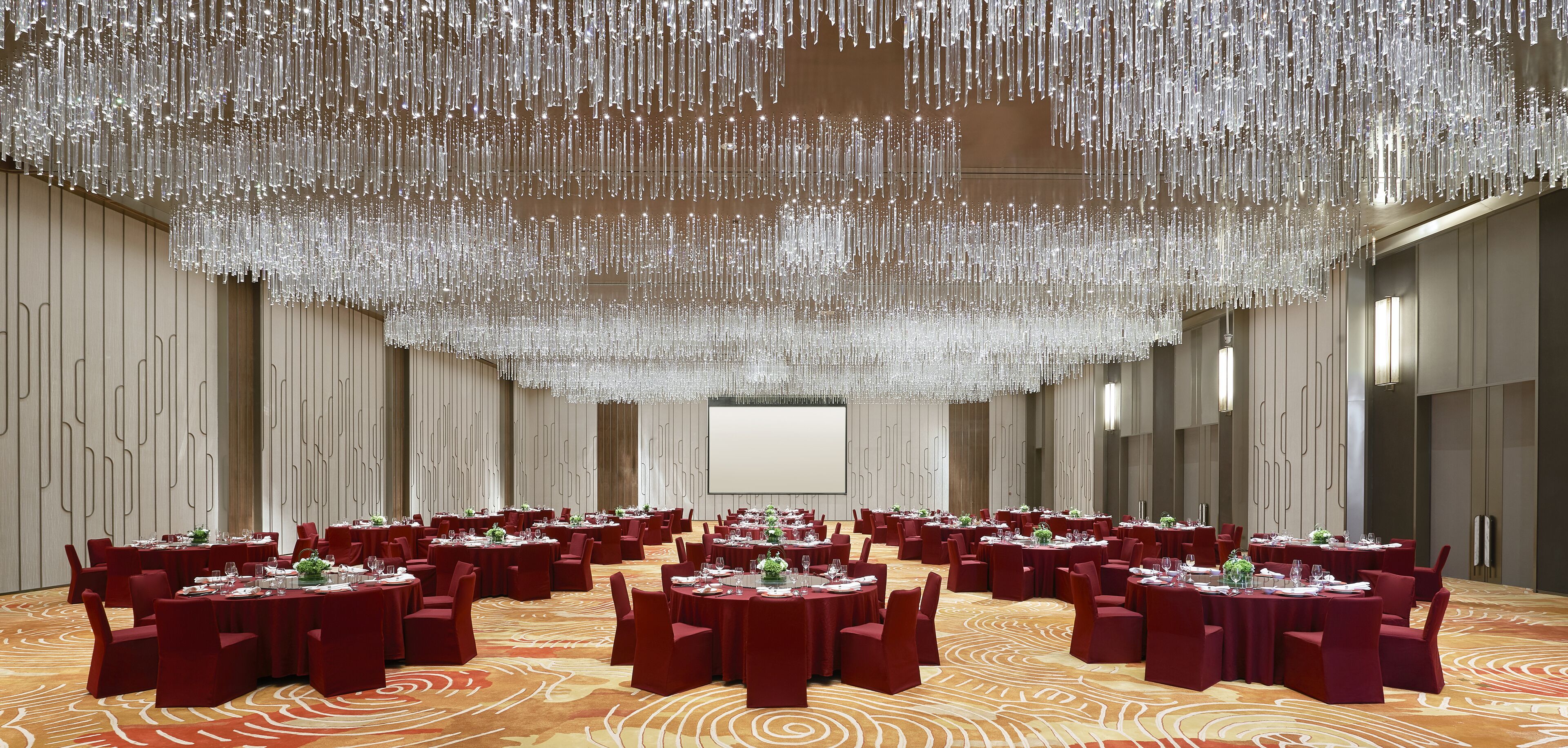 A large conference room with round tables, red chairs, and a chandelier.