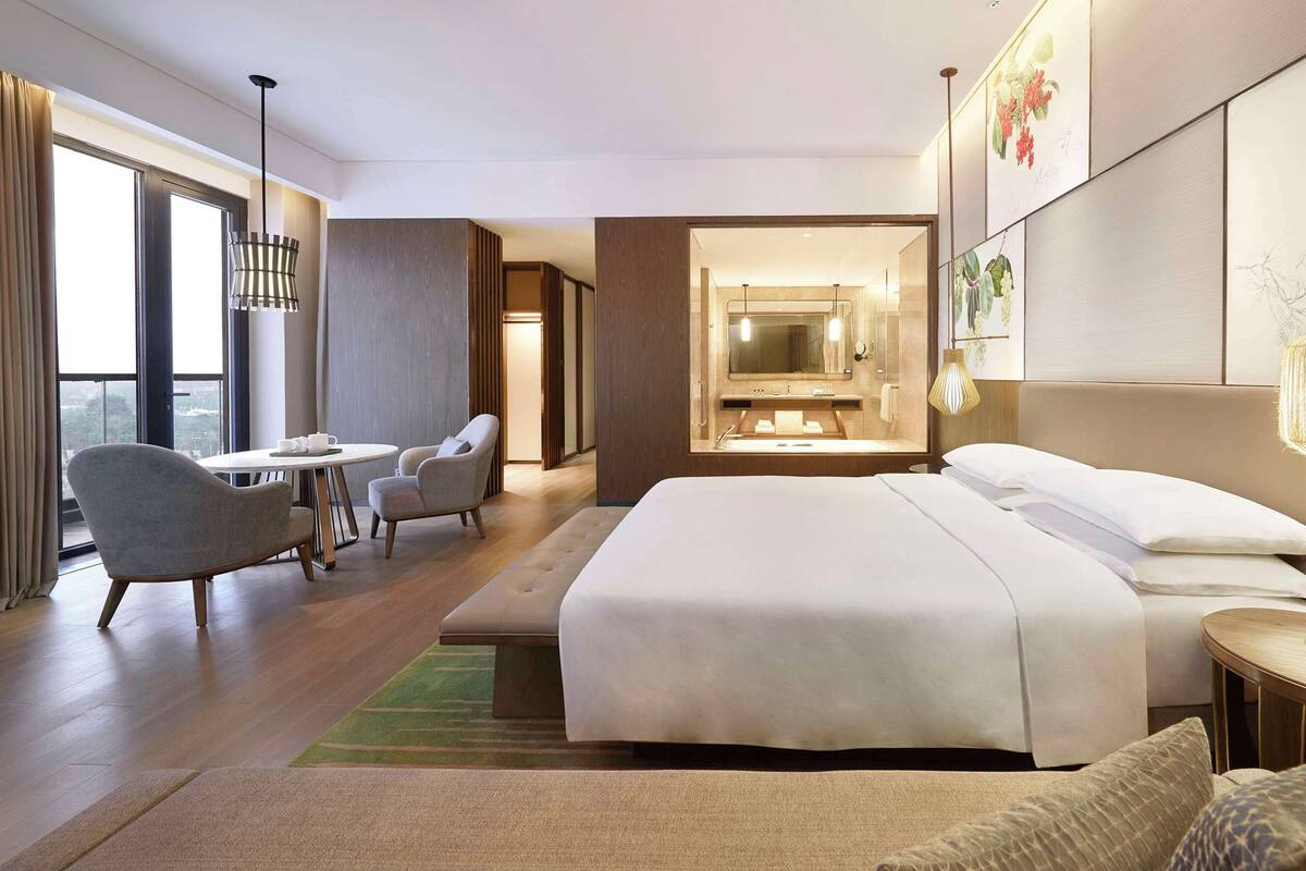 A hotel room with a bed, a desk, a chair, a bathroom with a mirror, and artwork on the walls.