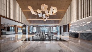 Een ruime lobby met een hoge plafond, moderne verlichtingsarmaturen en een fontein in het midden.