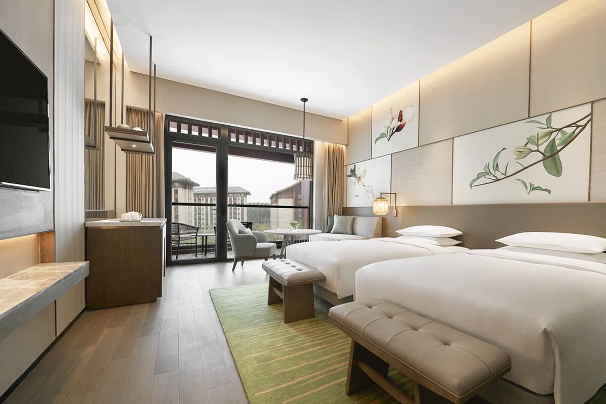 A modern hotel room with a balcony, a desk, two beds, and artwork on the walls.