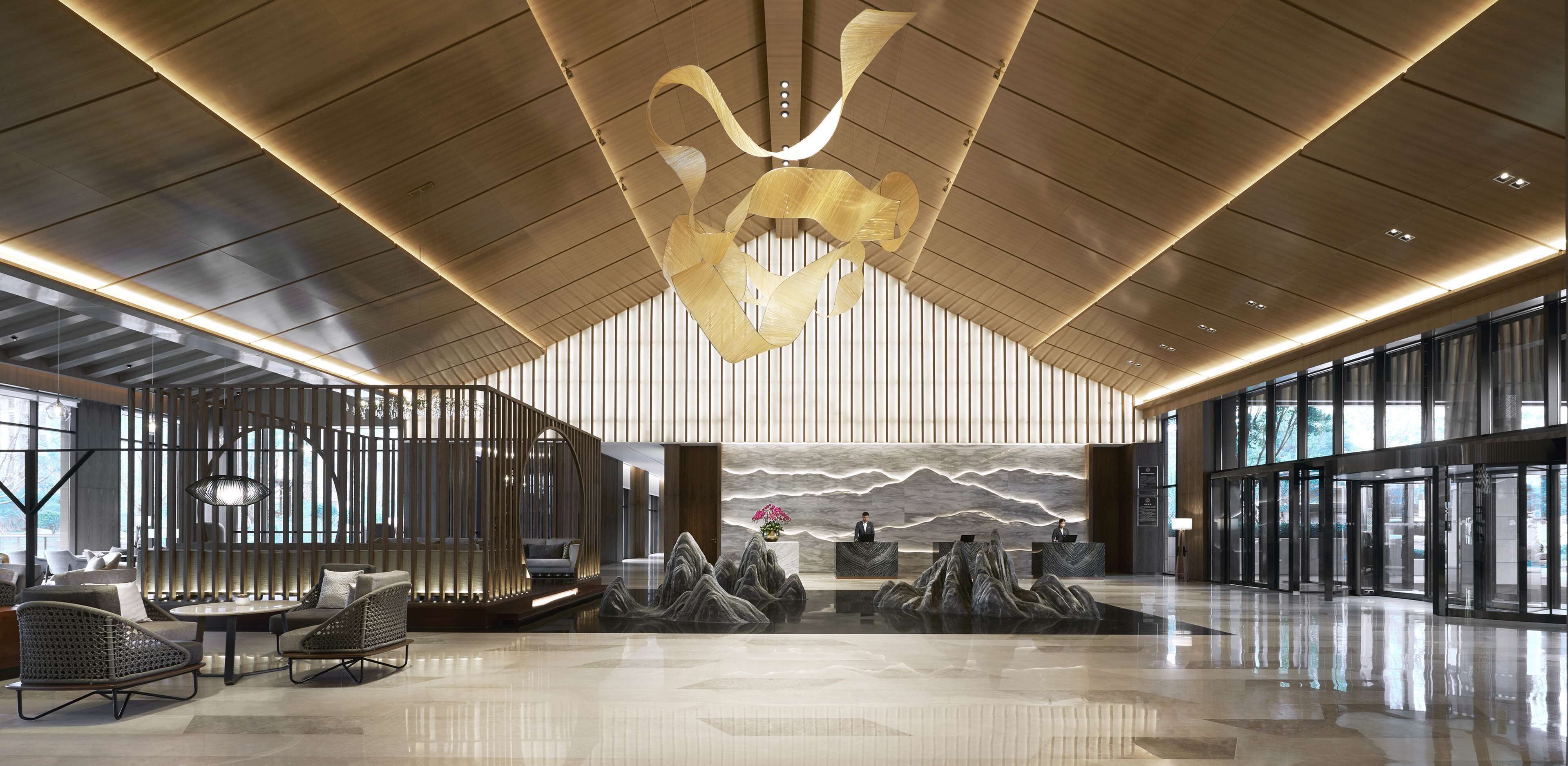 A spacious lobby with a high ceiling, modern reception desk, seating area, and large windows allowing natural light.