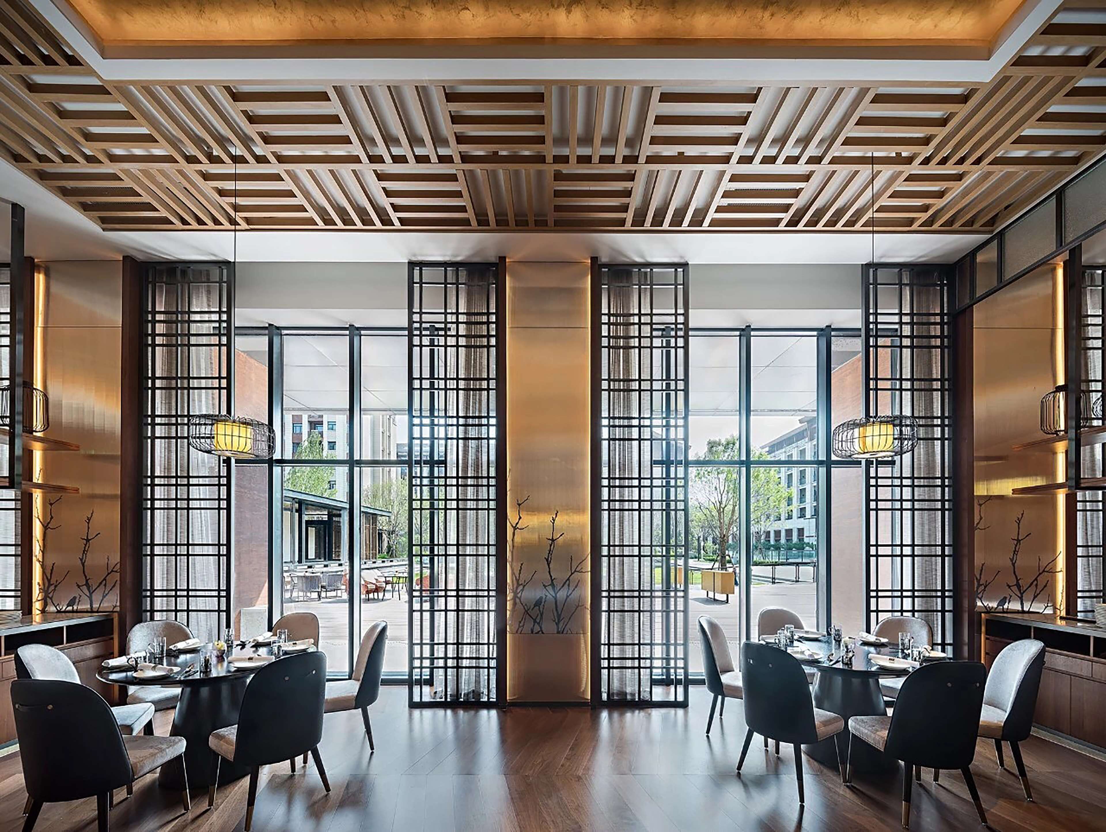 Un espace de restauration moderne avec des panneaux de plafond en bois, de grandes fenêtres dotées de grilles métalliques et un mobilier contemporain.