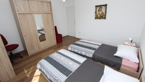 Un dormitorio con dos camas individuales, un armario de madera, una silla roja y una mesita de noche con una lámpara.