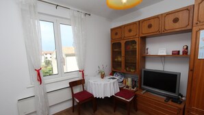 Una habitación con un armario de madera, televisor, mesa con sillas y ventana con cortinas.