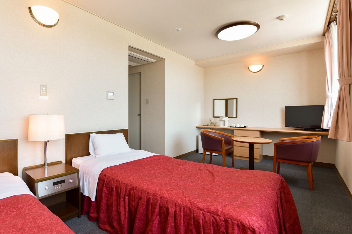 Habitación de hotel con dos camas, un escritorio, una silla, un televisor y un espejo.