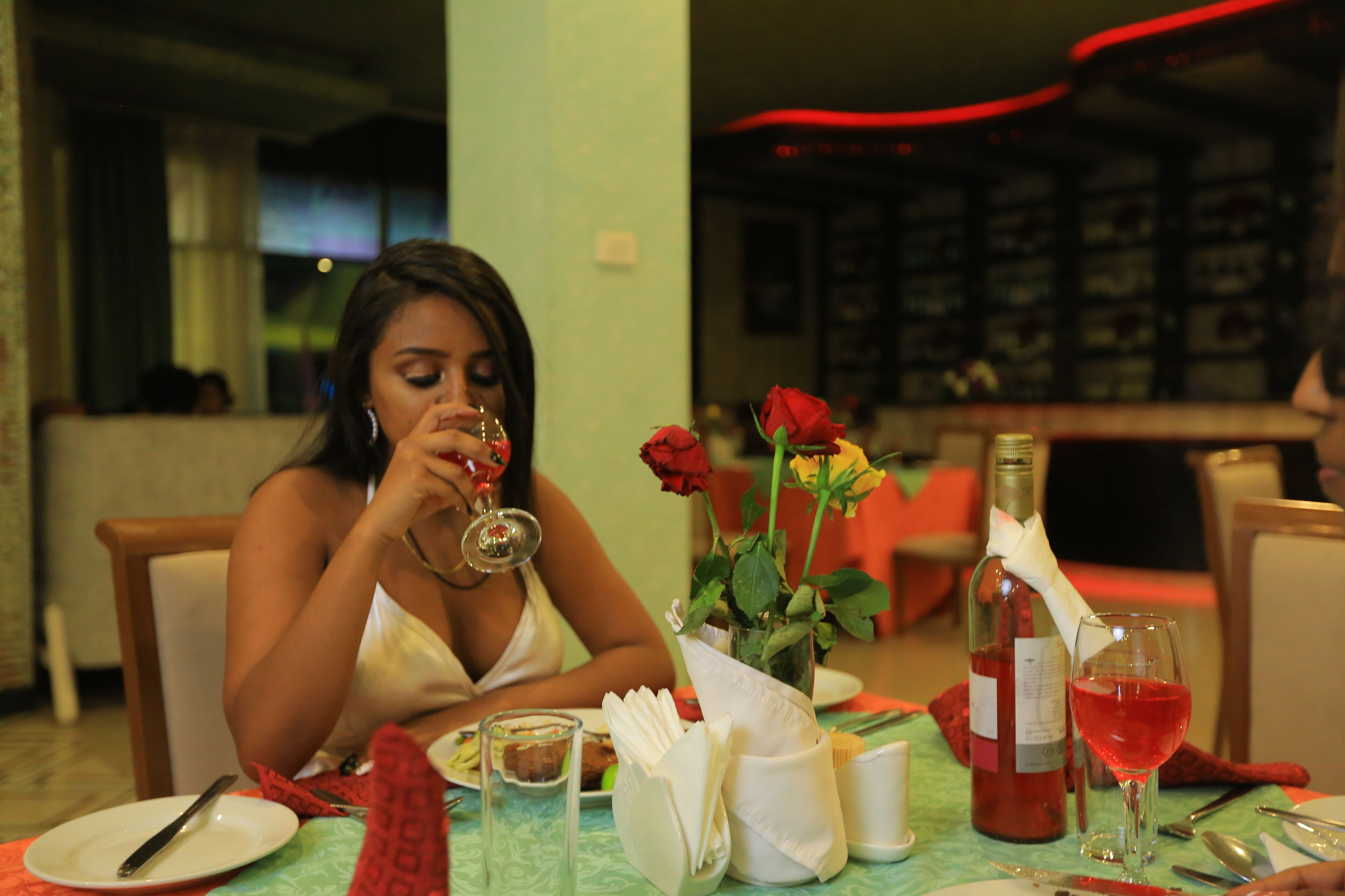 A dining table with a wine bottle, a glass of red wine, and a vase with roses.