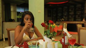A dining table with a wine bottle, a glass of red wine, and a vase with roses.