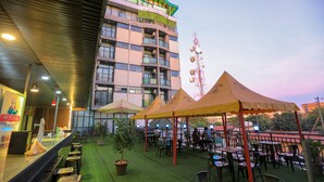 Een terras met tafels en stoelen, een bar en een gebouw met meerdere verdiepingen en balkons.