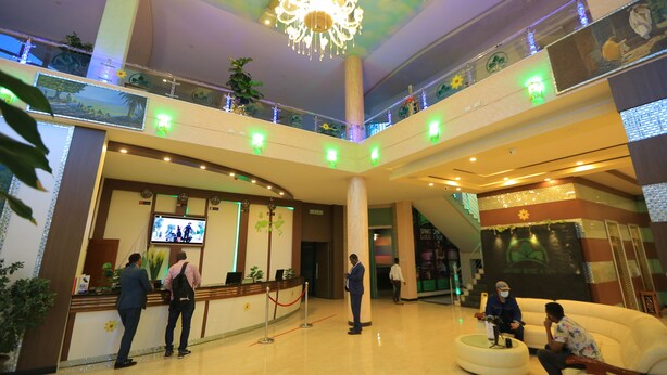 Een hotel lobby met een receptiebalie, een kroonluchter, meerdere verdiepingen en een zithoek.