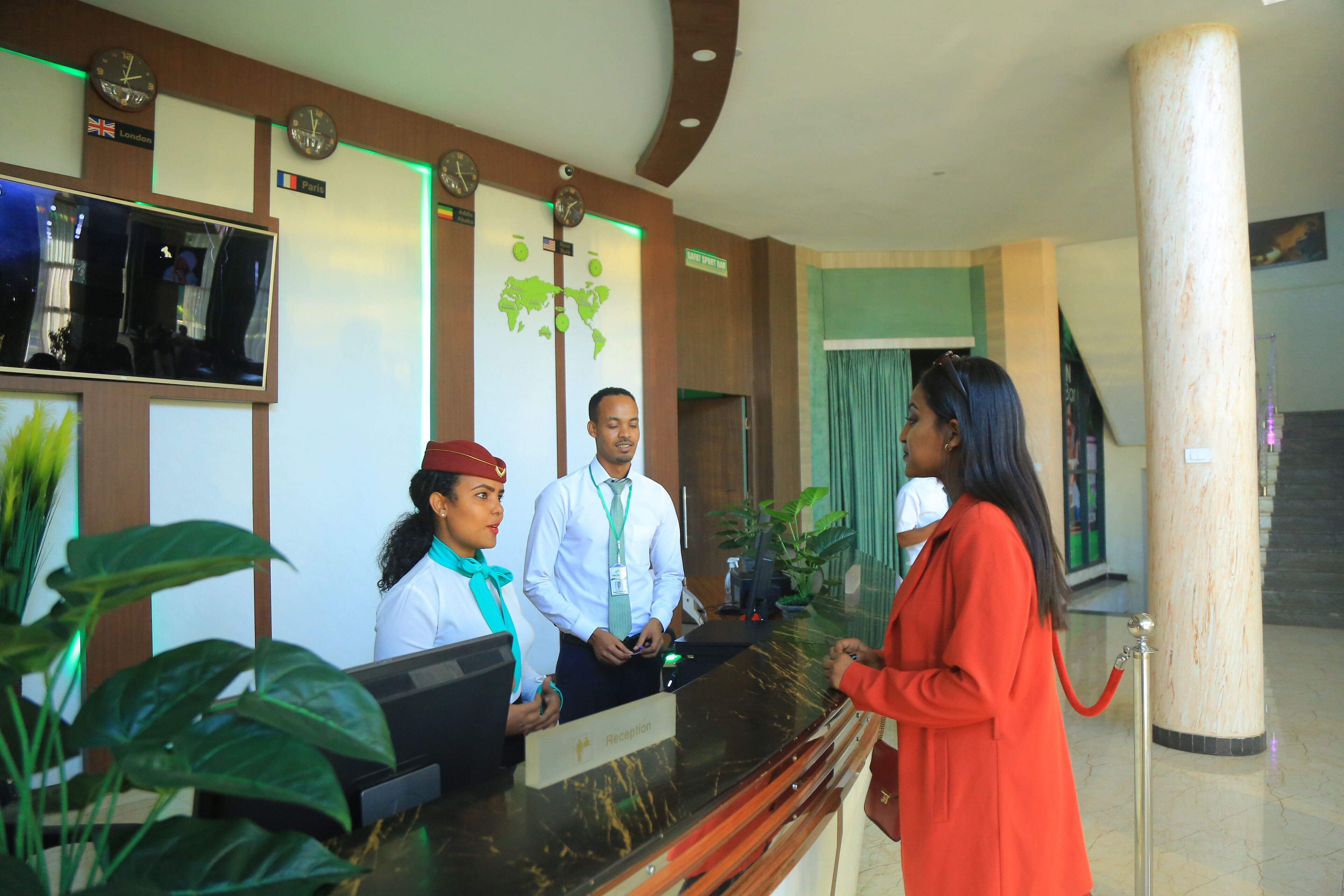 A hotel reception area with a reception desk, a world map, clocks, and a television screen.