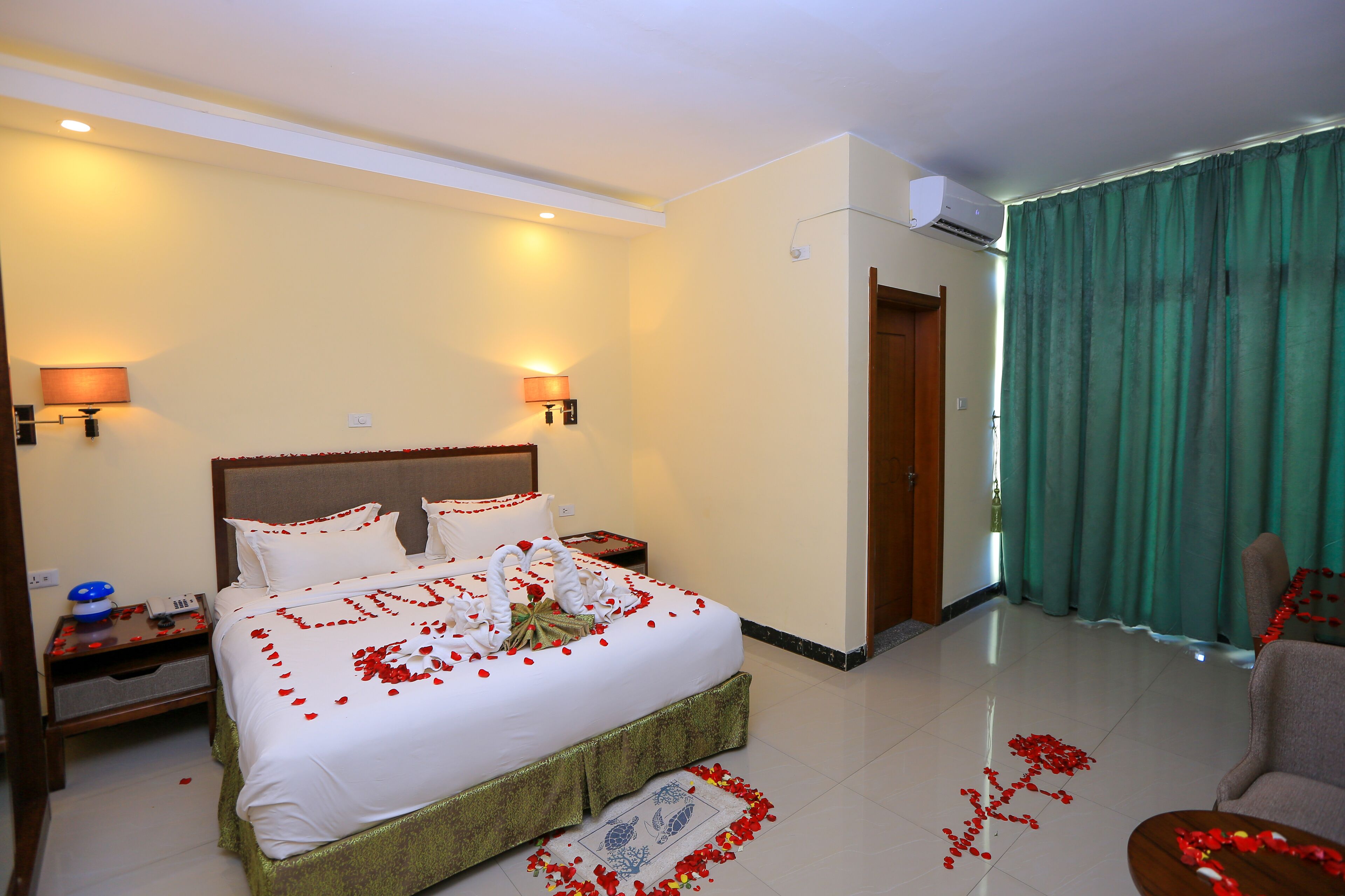 A hotel room with a large bed, two bedside tables, a nightstand, a chair, and a green curtain.