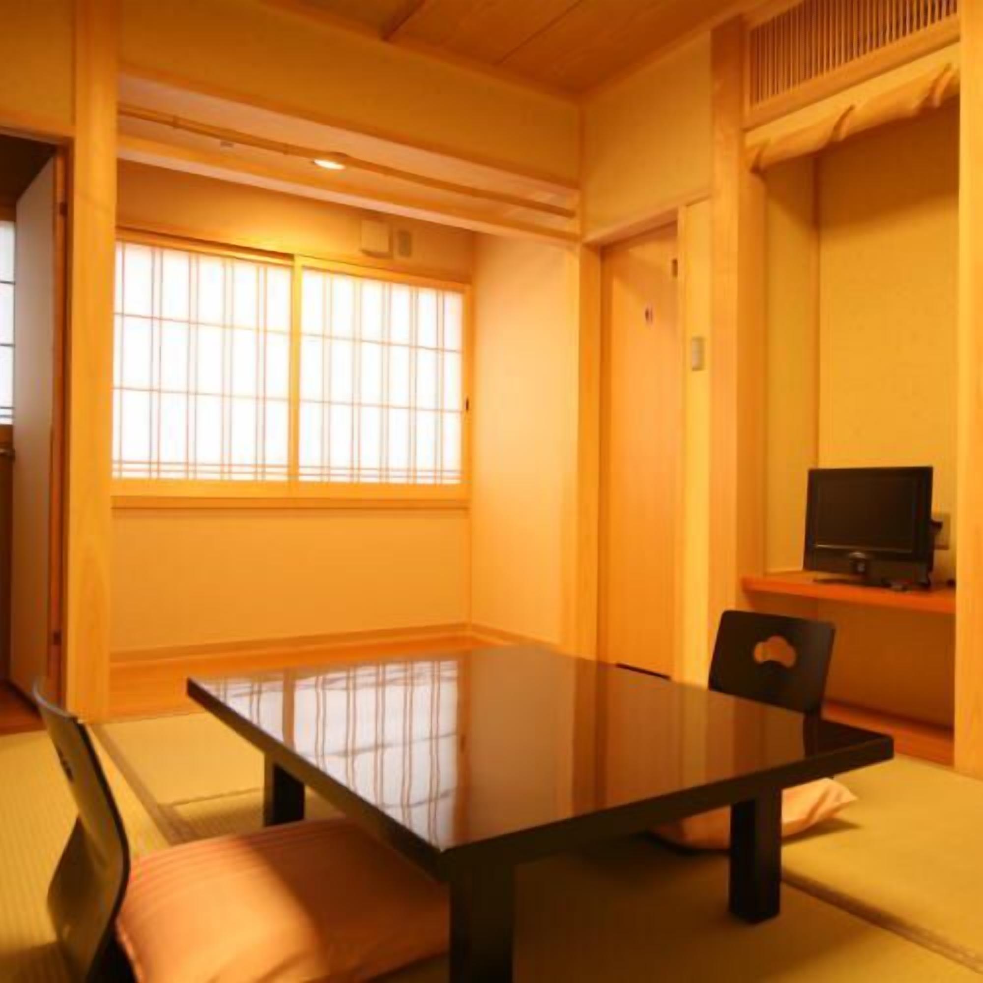 A room with a large window, a table, a chair, and a television.