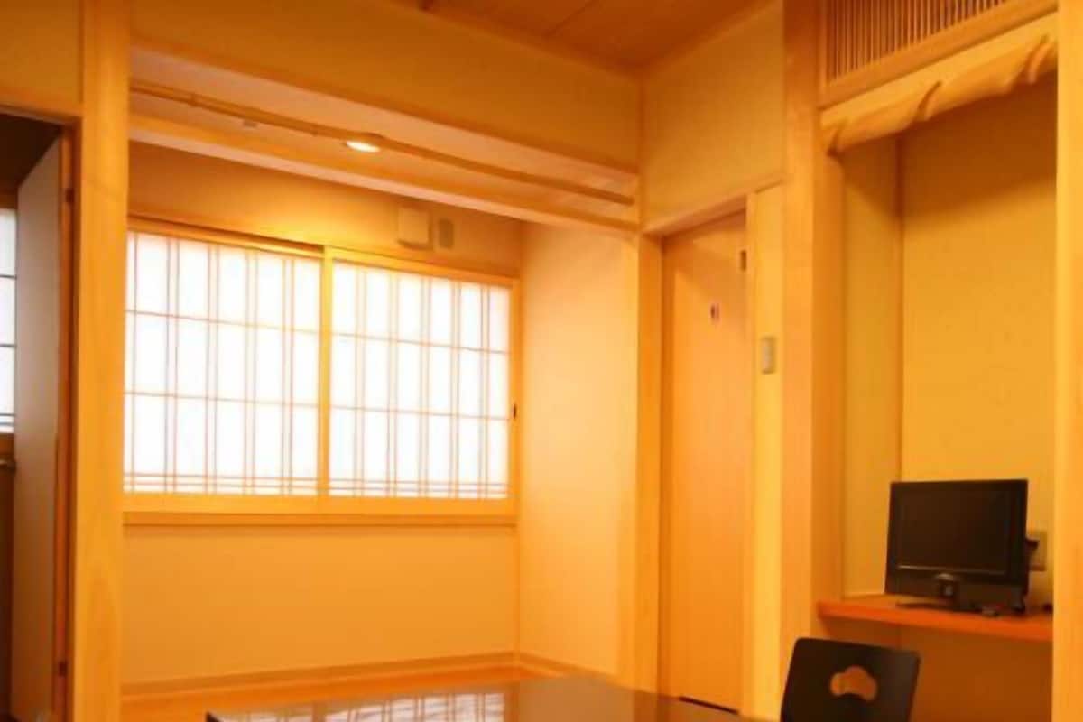 A room with a large window, a table, a chair, and a television.