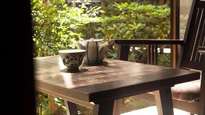 A table with a teapot and a cup, a chair, and a view of greenery outside.