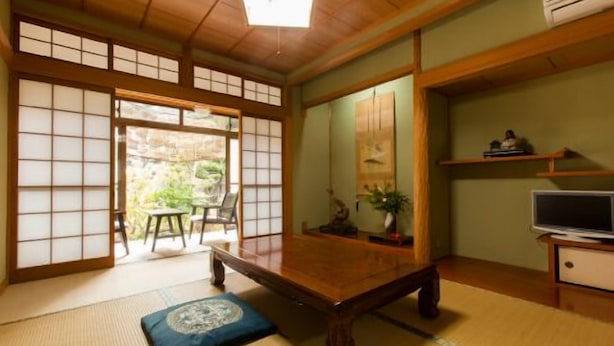 A traditional Japanese room with tatami flooring, a low table, sliding doors, and a television.