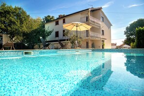 A swimming pool with tiled flooring, a building with a balcony, and outdoor furniture. - Apartments Villa Fjord (Kanfanar)
